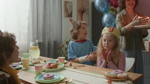 Garota soprando velas no bolo de aniversário, sentada com amigos na mesa festiva