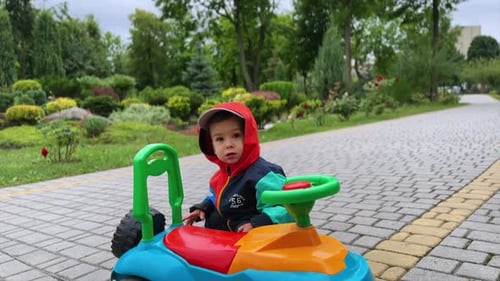 Lovely cute baby boy in jacket and hood stands near his toy car.