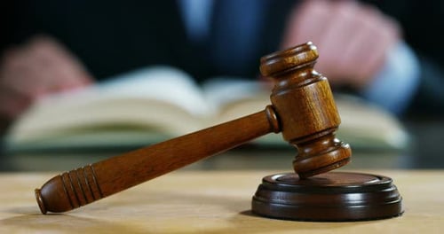 Wooden Gavel on a Table with Judge Reading