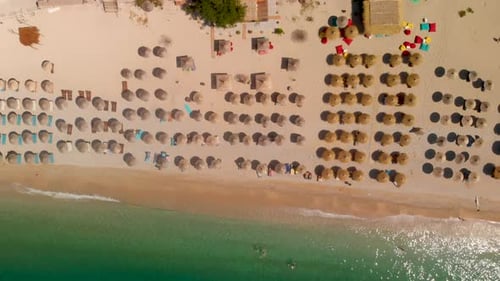 Slow aerial overhead flight over many umbrellas and waves at stunning sand beach