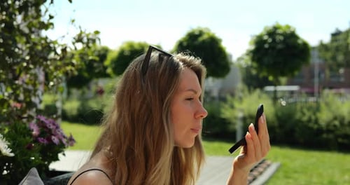 Woman with Sunglasses Looks Attentively in Mirror in Garden