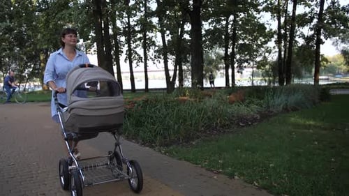 A Young Mother Walks in the Park with a Stroller