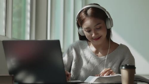 Happy young Asian student girl listening music and using laptop in university campus.