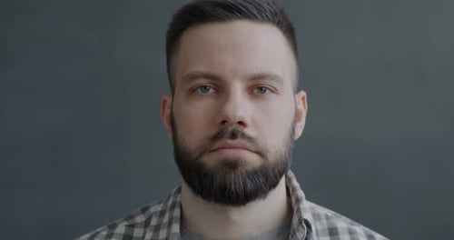 Slow Motion Portrait of Young Man Looking at Camera with Serious Expression on Gray Color Background