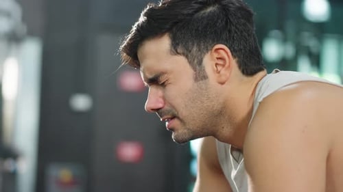 Exhausted Caucasian young sportsman trainer exercise in fitness club.