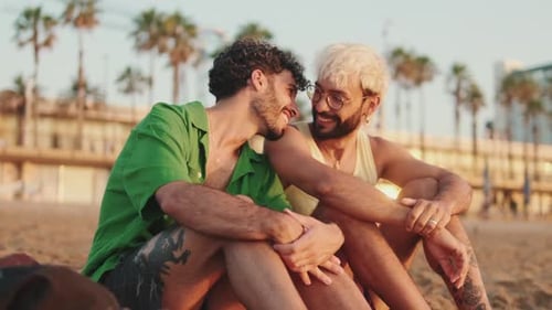 Casal homossexual apaixonado conversando sentado na praia ao nascer do sol