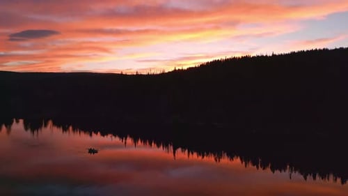 Aerial view of colorful sunset reflecting in lake with boat floating