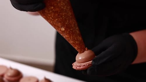 Close up of chef hands putting salt caramel with nuts in ganache cream on chocolate macarons shells.