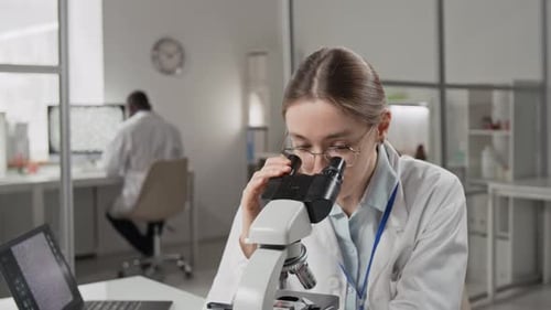 Scientist Uses Microscope in Lab With Colleague