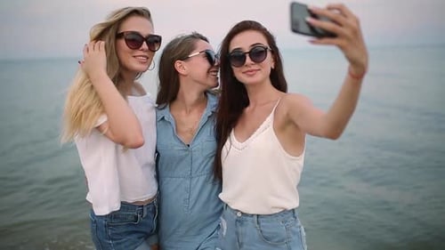 Three Young Women Taking a Selfie on the Beach with a Sea View Friends are Smiling Looking at the