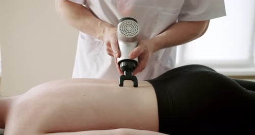 Masajista corporal masajeando la espalda de una mujer con masajeador de percusión
