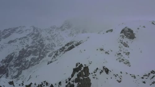 Schneesturm in den Bergen mit Nebel über den felsigen Hügeln, Luftaufnahme in 4k
