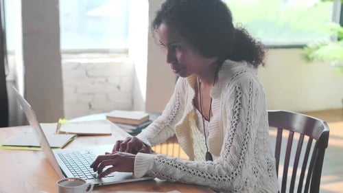 Young African American Woman Works with Laptop Sits at Table in Home Office