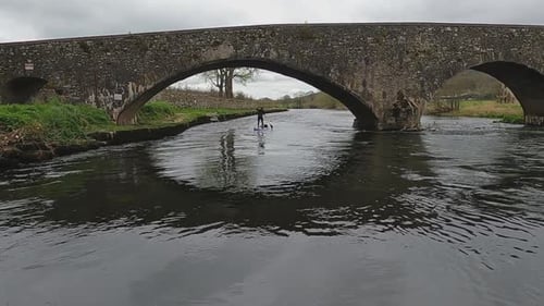 Paddleboarder paddles under old stone bridge near Tikincor Castle, IRE