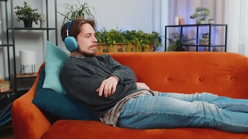 Happy Man in Wireless Headphones Relaxing Listening Favorite Rock n Roll Music Lying on Home Couch