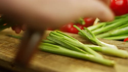 A Man Skillfully Cuts Fresh Green Onions with a Large Knife