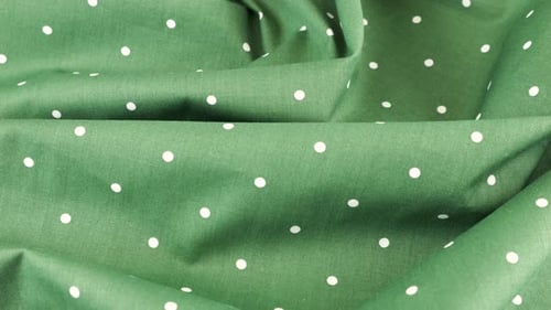 Top view of the soft folds of hooker's green with white polka dots cotton fabric rotated