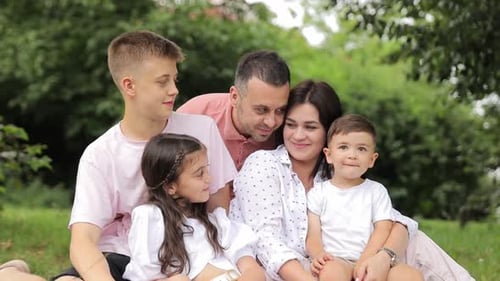 A Happy Family is Sharing a Leisure Moment on the Grass in a Park The Toddler is Making a Cute