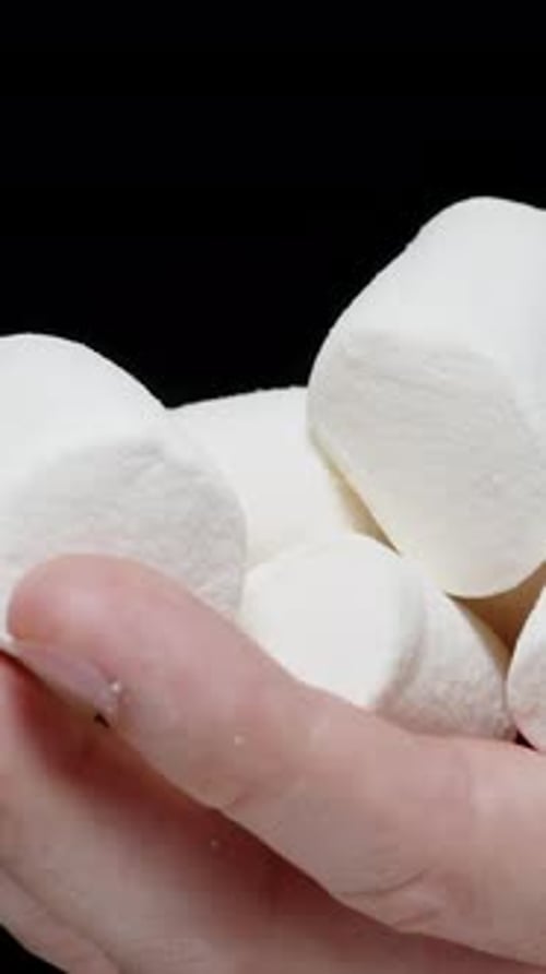 Vertical video. Close-Up of Male Palm with Many Marshmallows Being Poured Down Against a Black