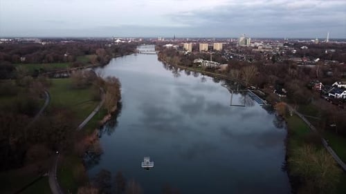 Langsame Luftaufnahme eines natürlichen Sees mit Pfad und Stadtlandschaft
