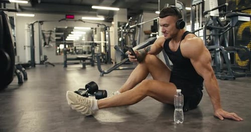 Athletic Man Resting in Gym Looking at Phone