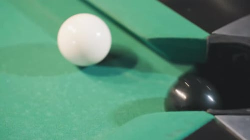 Black Billiard Ball Rolling Toward Pocket After White Cue Ball Strike