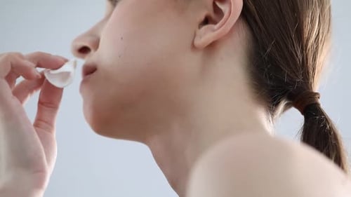 Artist removing makeup from woman's face indoors, closeup