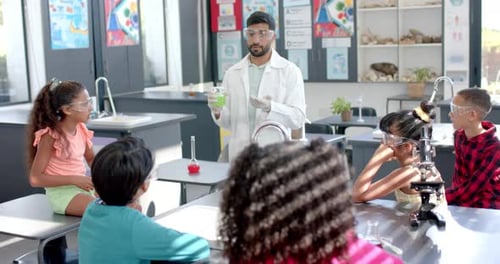 In a school classroom, a biracial teacher demonstrates a chemistry experiment