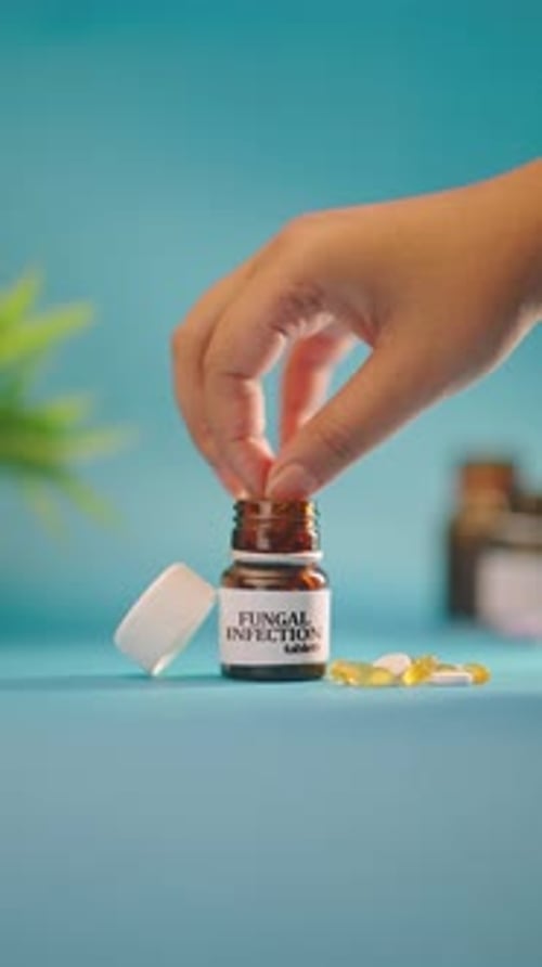 Hand Placing Pill in Fungal Infection Tablet Bottle