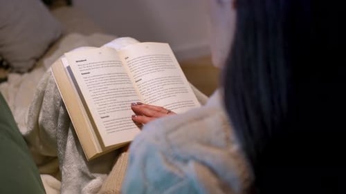 Eine Frau blättert eine Seite in dem Buch um, das sie bequem auf der Couch liest