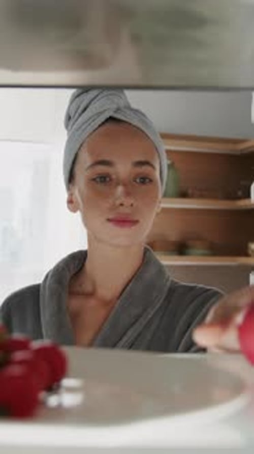Woman in robe looks in refrigerator for apple