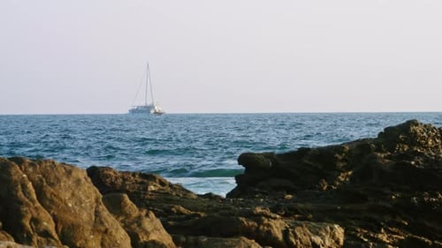 Segelboot navigiert über riesigen blauen Ozean Weiße Segel gegen klaren Himmel Wellen stürzen an felsiger Küste ab Hinweis auf