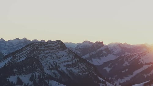 Witness the enchanting sunrise casting a golden glow on the silhouette of a snow-covered mountain ra