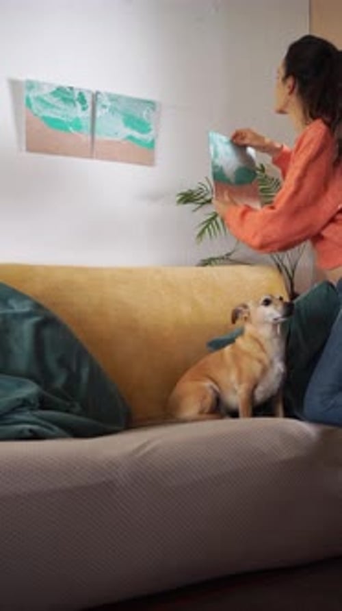 Woman hangs art with her dog on couch