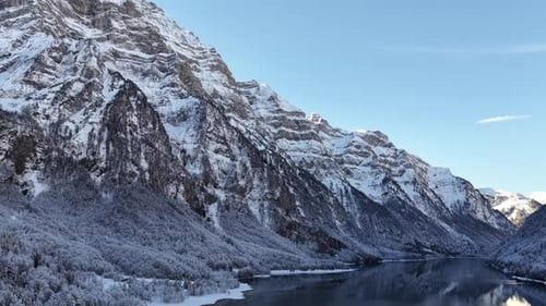 Aerial view of a frozen alpine lake surrounded by snow-covered mountains, captured on a clear