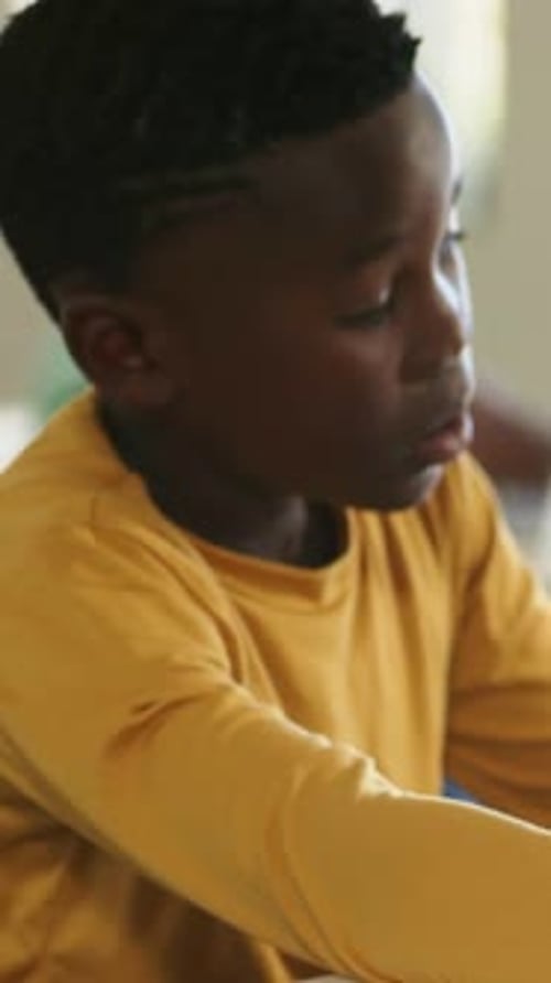 Vertical video: Lifting after resting, boy in mustard shirt studying at school desk with notebook