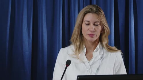 Woman Speaking at Podium in Front of Curtain