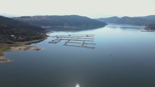 Aerial shot of organized fish farms floating on the calm waters of a reservoir, surrounded by mounta