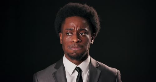 African Man in Smart Suit Stands Over Black Background in Studio Looking Directly at Camera with a
