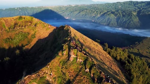 Crête volcanique au-dessus de la caldeira avec des randonneurs traversant un chemin exposé au lever du soleil sur le mont Batur, vue aérienne