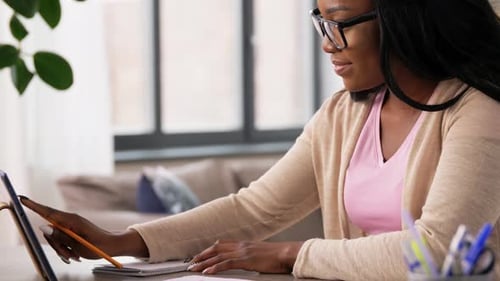 Woman Designs on Tablet, Writes Notes at Desk