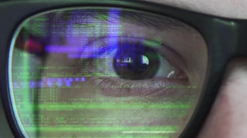 Close up view of a coding text reflecting on the glasses in green color with blue highlights in the