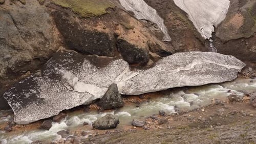Fixed view of the river descending from Brennisteinsalda in Landmannalaugar, Iceland, with a block o