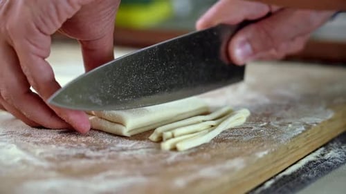 Hands cutting dough into noodles
