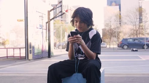Preteen Boy with Headphones Using Smart Phone on City Basketball Court 1213 Years