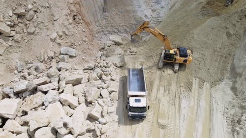 Aufnahme eines gelben Kettenbaggers, der den Muldenkipper mit Sand auf der Baustelle belädt, Drohnenansicht von