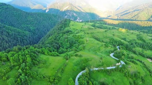 A Road Passes Hills Covered with Spruce Forests and Meadows Against a Cloudy Sky