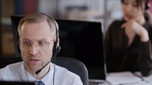 Male Operator Speaking via Headset Working in Call Center with Colleagues