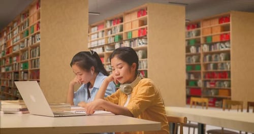 Students With Headphones Are Bored Reading The Books While Sitting On The Table In The Library