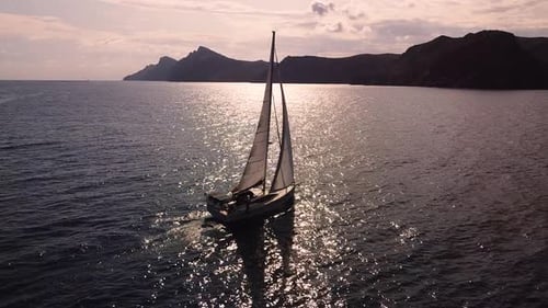 Sailboat sailing by coastline seashore against sunset and mountains. Sail boat in the south coast